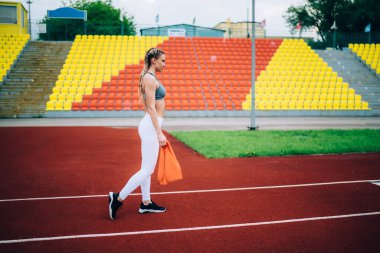 Modern sportif formda genç bir kadının, renkli tribünlere karşı şehir stadyumunda ayakta dururken lastik bant takması ve sağlıklı bir yaşam sürmesi.