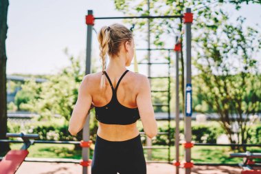 Genç zayıf atletik kadın, sarı saçlı, siyah spor kıyafetli yazın spor salonunda spor yapıyor.