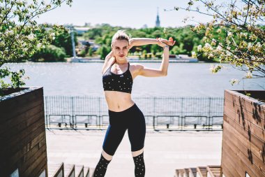 Siyah şık giyinen çekici bayan atlet ayakta ve ellerini başının arkasına uzatarak ve bulanık arka planda yaz rıhtımından uzağa bakarak. 