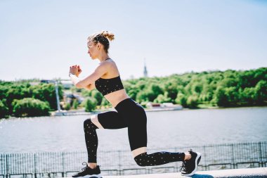 Aktif enerjik kadın eğitiminin, çömelmiş bacağının ve nehir boyunca beton çitin üzerinde göğüs hizasında el ele tutuşmanın yan görüntüsü