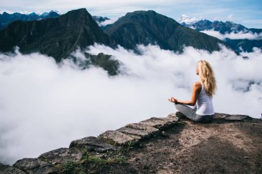 Machu Picchu 'nun zirvesinde sakin ve ilham verici, rahat kadın turist lotus pozisyonunda oturuyor ve doğal çevrenin manzarasına hayranlık duyuyor huzur dolu bir yerde yoga meditasyonu sırasında ahengi hissediyor.