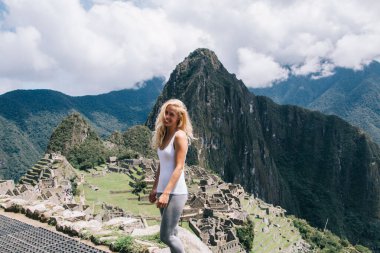Yüzünde en tatlı gülümsemeyle, Machu Picchu yakınlarındaki doğal çevreyi keşfetmek için yürüyüş yapan, tasasız, yeşil manzarada mutluluğu hisseden neşeli kadın yürüyüşçünün yarım boy portresi.