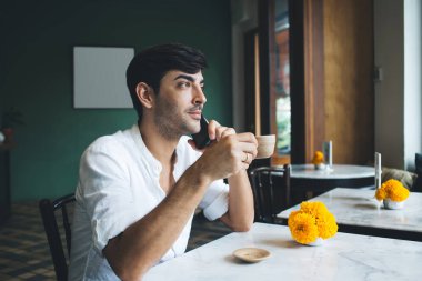 Beyaz gömlekli yakışıklı erkek girişimci, rahat kafeteryada sabah kahvesinin tadını çıkarıyor. Masasında sarı çiçekler, tatilde cep telefonuyla konuşan dalgın iş adamı.