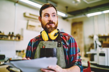 Elinde taslak olan yakışıklı genç adam kendi atölyesinde mobilya yapmaya hazırlanırken başka yöne bakıyor.