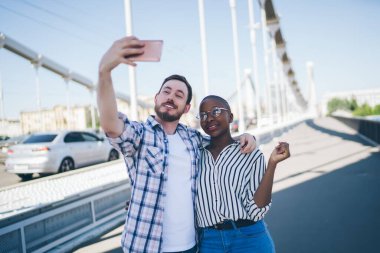 Gömleği kollu yakışıklı adam cep telefonuyla selfie çekti. Kısa saçlı, Afro-Amerikalı bir kadına sarıldı.