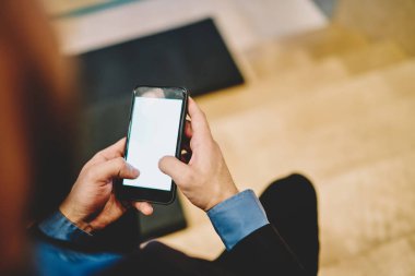 Resmi kıyafetli mahsul adamın, modern binanın çalışma alanındaki sosyal medyayı kontrol etmek için akıllı telefon kullanarak ara vermesine yukarıdan bak