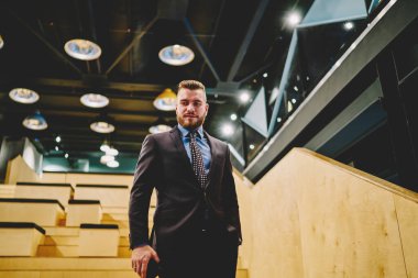 Modern binanın merdivenlerinde dikilip bakışlarını kaçıran zarif takım elbiseli başarılı, sakallı genç adamın manzarası. 