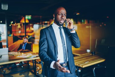 Sorunlu Afro-Amerikan zeki iş adamı. Katı mavi takım elbiseli, kol saati takan, modern ofiste cep telefonundan konuşan.