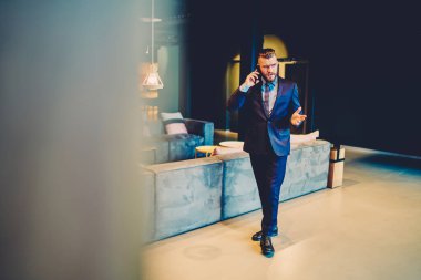 Ciddi bir işadamı cep telefonuyla konuşuyor ve ofis salonunda beklerken kolundan memnun olmayan bir jest yapıyor.