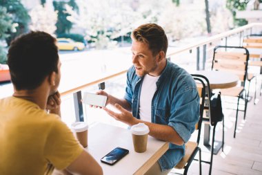 Kafeteryada erkek arkadaşıyla buluşurken akıllı telefondan uygulamayı gösteren neşeli beyaz adam. Çalışanlar vide 'ı izlemek için cep telefonu kullanarak ortak girişimi tartışıyor.