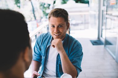 Modayı takip eden beyaz tenli yakışıklı adamın yarım boy portresi iş arkadaşıyla kahve molası verirken kameraya bakıyor, kendine güvenen erkek girişimci partnerle planlarını tartışıyor.