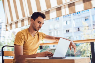 Kendine güvenen erkek öğrenci dizüstü bilgisayarda öğrenim kursunu seyrediyor, terasta oturuyor, ciddi yetenekli serbest çalışan adam uzaktan kumandalı görevler üzerinde kafa yoruyor, e-postaları ve Exchang haberlerini kontrol ediyor.