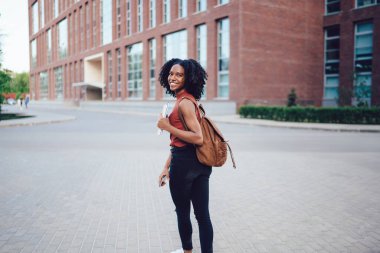 Neşeli, Afro-Amerikan kıvırcık saçlı, kolsuz tişörtlü, sırt çantası ve kitaplarıyla yaz aylarında el ele yürüyen kadın.