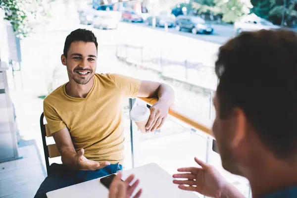 Cheerful caucasian male friends having funny conversation and discussion during coffee break on summer day, happy hipster guys talking and talking to each other gesturing on free time meetin