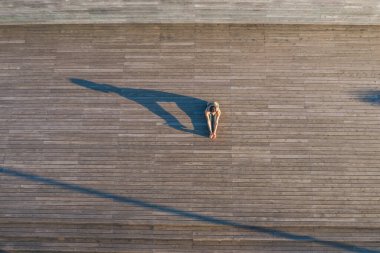 Tanınmayan aktif bir kadının kollarını bacaklarının arasına dayayıp esneklik göstermesi ahşap zeminde oturup yoga yapması.