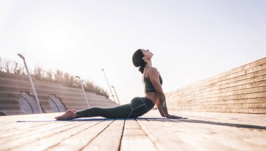 Kobra yoga pozisyonunda rahat spor giyimli huzurlu bir kadın parlak güneş ışığında minder üzerinde pratik yapıyor.