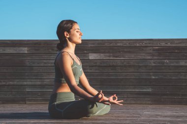 Nilüfer çiçeği pozisyonunda sakin bir kadın, dizlerinin üzerinde elleri ve gün doğumunda ahşap patikada gözleri kapalı.