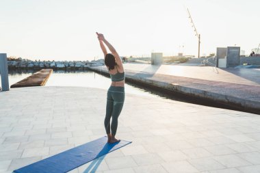 Yeşil spor giyim tarzında tanınmayan bir kadın, yoga yapıyor ve kollarını mavi mindere uzatıyor.