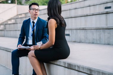 Resmi tarz takım elbiseli ve gözlüklü zeki Asyalı yönetici dışarıda stadyumun sallanan tribününde otururken meçhul kadın yöneticiye danışmanlık yapıyor. 