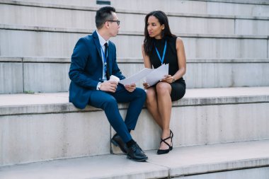 Resmi olarak çok ırklı erkek ve kadın iş ortakları açık hava stadyumunun tribününde otururken belgelerle strateji oluşturuyorlar. 