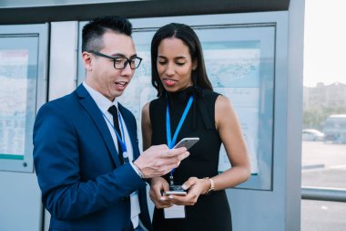 Şirket ekibi, ofis binasının dışında ellerinde cihazlarla ayakta duruyor ve yüzünde gülümseme olan akıllı telefon ekranına bakıyor.