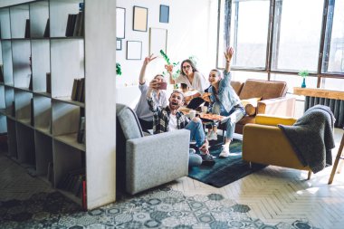 Geniş bir oturma odası. Mutlu, arkadaş canlısı bir grup genç, gülümseyip cep telefonuyla selfie çekerken masada, koltukta ve yerde bacak bacak bacak üstüne atarak pizza yiyor. 