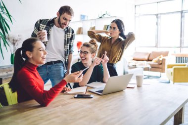 Bir grup genç gülüyor ve ödevlerini tartışıyorlar. Bu sırada da dizüstü bilgisayarla masanın etrafında toplanıyorlar ve rahat bir dairede ödev yapıyorlar.