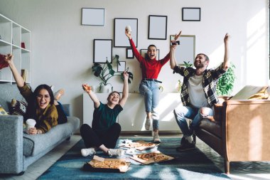 Mutlu heyecanlı genç arkadaşlar ifade ile el kaldırıyor pizza yiyor ve içecekler içiyor modern oturma odasında dinleniyor ve arka planda boş fotoğraf çerçeveleri var.