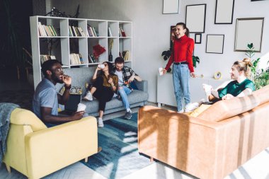 Günlük giysiler içinde gülen genç bir bayan dinlenme odasının ortasında şaşkın ve neşeli çok ırklı arkadaşlar rahat koltuklarda oturuyor.