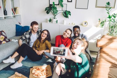Gündüz vakti pizzanın yanında oturan ve akıllı telefonuyla selfie çeken çok ırklı yetişkin insanlara gülüyorlar.