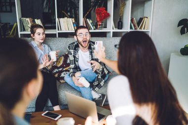 Genç, şaşkın, ağzı açık bir şekilde cep telefonuna bakan genç bir hippi. Bu sırada isimsiz esmer, arkadaşlarıyla oturma odasındaki internet haberlerini paylaşıyor.