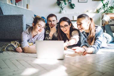 Genç arkadaşlar dizüstü bilgisayarda internette gezinip evdeki rahat oturma odasında birlikte yatıyorlar.