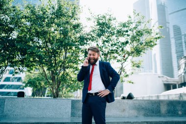 Koyu renk takım elbiseli, kırmızı kravatlı, enerjik, zeki bir adam iş merkezinde cep telefonuyla coşkulu bir şekilde konuşuyor. 