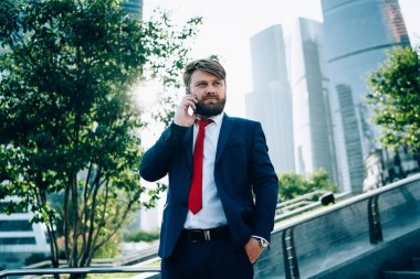 Koyu renkli şık takım elbiseli ve kırmızı kravatlı düşünceli bir işadamı cep telefonuyla konuşurken dikkatle dinliyor. 
