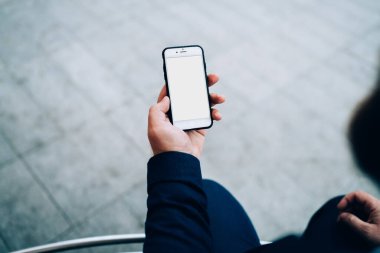 Yukarıdan gelen boş cep telefonu ekranında asfalt yolda oturan koyu renk elbiseli bir mahsul var. 