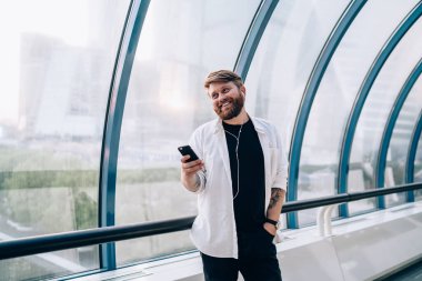 Siyah tişörtlü, beyaz tişörtlü, gülümseyen bir adam cep telefonuyla konuşuyor ve açık geometrik tünelde pencereye bakıyor.