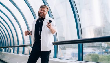 Halka açık bir yerde neşeli ruh hali içinde dans eden mutlu hipsterin yarım boy portresi akıllı telefon uygulaması ve elektronik kulaklıkla müzik listesi dinlerken, neşeli adam boş zamanlardan zevk alıyor.