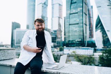 Gömleği kollu, karizmatik serbest çalışan, yuvarlak gözlüklü, işten dinlenen telefonlara sarılıp iş yerindeki kameralara bakan biri.