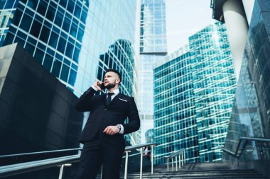 Siyah takım elbiseli bir adam mermer merdivenlerde dikilirken arıyor Metropolis 'teki cam aynalı binaların arka planında