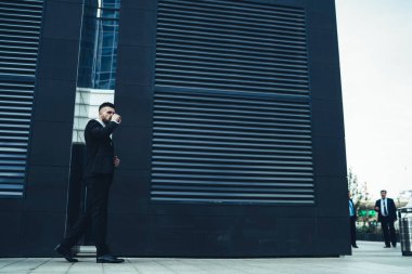 Tam teşekküllü girişimci sıcak içeceğini yudumlarken ve kaldırımda yürürken şehir caddesindeki modern binanın önünde yüzünü çevirirken.