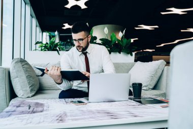 Kırmızı kravatlı ve gözlüklü kendine güveni tam bir adam kahve barında oturmuş menüyü kontrol ederken dinleniyor.