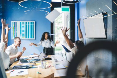 Resmi kıyafet giymiş heyecanlı bir Afrikalı Amerikalı kadın ellerini kaldırıp boş ekran ve çizelgelerle masa başında otururken tezahürat yapıyor.