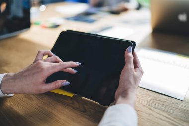 Ofisteki ahşap masada otururken, beyaz bluzlu, manikür gözleme tabletli zarif bayanın seçici odağı.