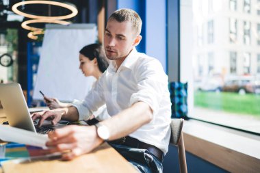 Bilgisayarda yazı yazarken ve evrak işleriyle uğraşırken modern ofiste masaya oturan düşünceli meslektaşlarımızın yan bakışları.