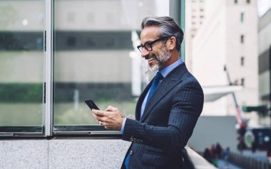 New York 'ta balkona yaslanıp cep telefonu kullanan sakallı ve gözlüklü orta yaşlı işadamının yan görünüşü.
