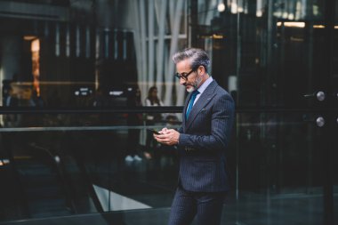 Gözlüklü, siyah kostümlü, modayla gezen ve New York 'ta cam duvar boyunca yürüyen modern ve modaya uygun bir iş adamının yan görüntüsü.