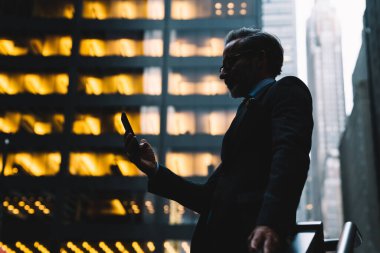 Orta yaşlı iş adamının gökdelenlerin gölgesinde duran ve New York 'ta akıllı telefonu elinde tutan görüntüsünden.