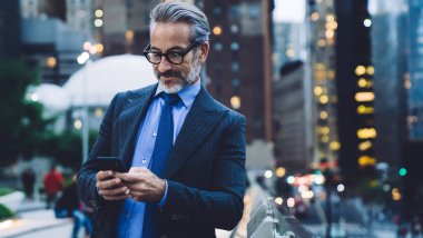 Yakışıklı, gri saçlı ve sakallı bir iş adamı. Siyah ceketli, mavi kravatlı ve gözlüklü. New York 'ta arka planda bulanık bir şekilde akıllı telefondan mesaj atan.