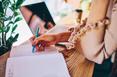 Günlük giysiler giymiş, günlük kıyafetlerini giymiş, not defterine notlar yazan, kafede dizüstü bilgisayarla çalışan, serbest çalışan bir kadın.