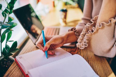 Gündelik giysiler içinde giyinen bayanın yukarıdan not defterine not alarak kafeteryada bilgisayarla çalışan uzak bir proje oluşturması.